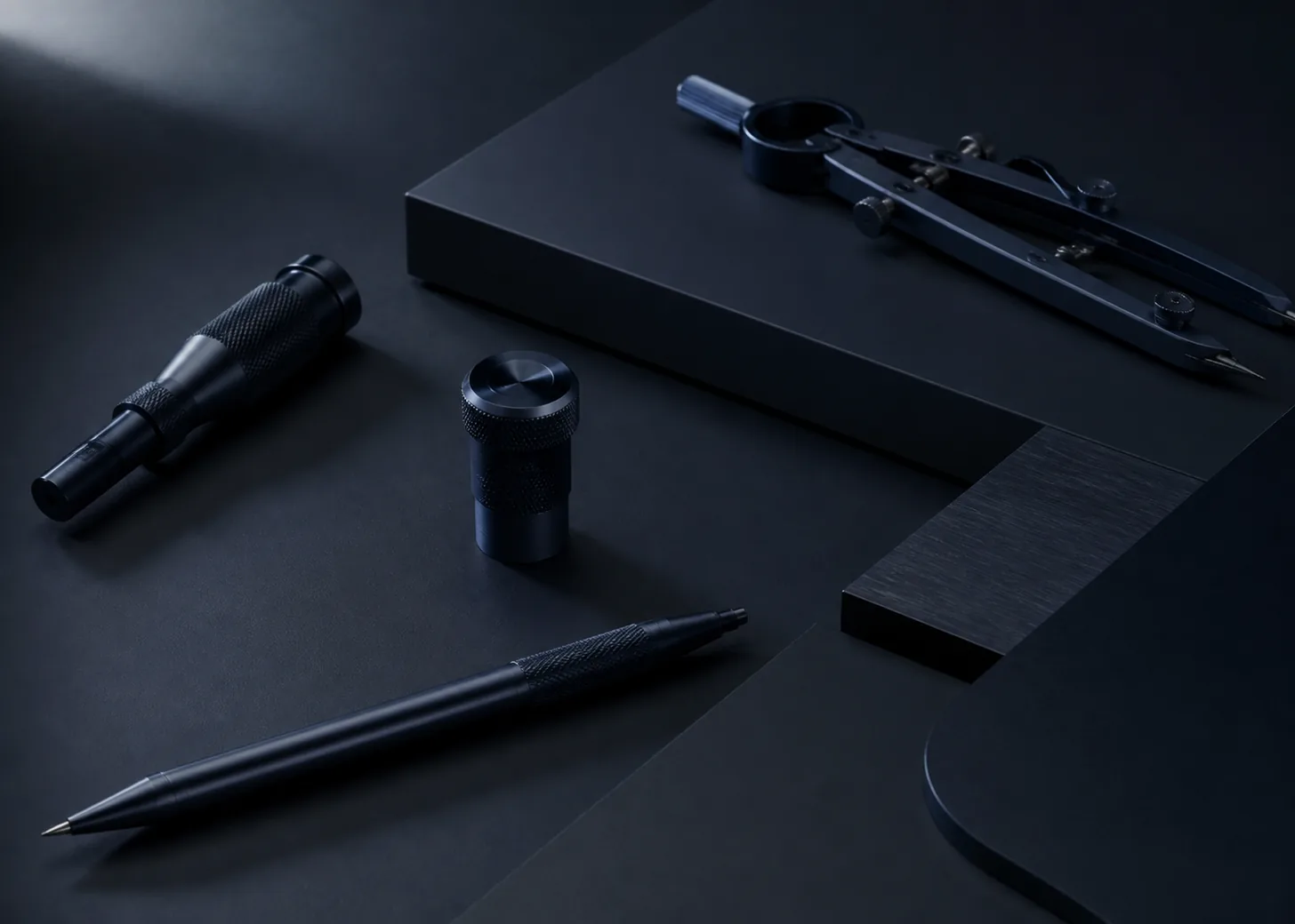 Near-black navy stationery, technical instrument, and dark metal fittings in side light